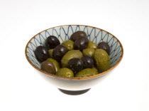 Food, Fruit, Olives, Ripe black and green olives Olea europaea in olive oil in a bowl against a white background.
