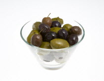 Food, Fruit, Olives, Ripe black and green olives Olea europaea in olive oil in a glass bowl against a white background.