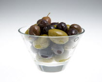 Food, Fruit, Olives, Ripe black and green olives Olea europaea in olive oil in a glass bowl against a white background.