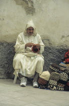 Morocco, Essouira, Man Knitting in Market.   