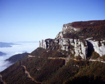 France, Rhone-Alpes, Isere, Les Aiguilles. Limestone cliffs and towers south west of Col de Rousset in the Vercor region with thick white cloud and mist lying across lower slopes.