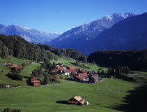 Switzerland, Bern, Brunigen, Small hamlet of Brunigen near town of Meiringen. Cluster of buildings in green valley surrounded by trees with mountain backdrop.