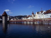 Switzerland, Luzern, River Reuss crossed by covered wooden footbridge Kapellbruche with Wasserturm on left and Jesuiten Kirche behind. Seen from Seebrucke.