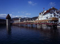 Switzerland, Luzern, River Reuss crossed by covered wooden footbridge Kapellbruche with Wasserturm on left and Jesuiten Kirche behind. Seen from Seebrucke.