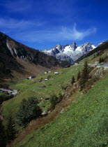 Switzerland, Uri, Susten Pass, View up to Susten Pass from near hamlet of Farnigen with the glaciers of Grassengrat Ridge on the skyline against blue sky with high windswept cloud.