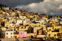 Mexico, Bajio, Zacatecas, Colourful houses clinging to the hillside below sky of thick, grey cloud.