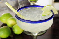 Mexico, Jalisco, Puerto Vallarta, Frosted glass of a margarita cocktail served with ice and slice of lime with whole limes at side.