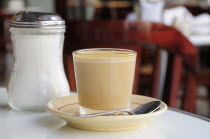 Mexico, Veracruz, Cafe con leche, coffee with milk served in glass with saucer and spoon, on table beside sugar canister.