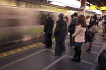 Japan, Tokyo, Commuters waiting on platform whilst train speeds through without stopping.