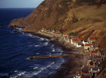 Scotland, Aberdeenshire, Crovie, One time fishing village seen from cliff top.  Row of cottages at foot of steep hillside overlooking coast and stone jetty.