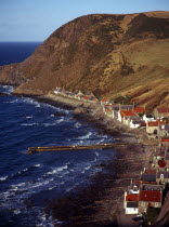 Scotland, Aberdeenshire, Crovie, One time fishing village seen from cliff top.  Row of cottages at foot of steep hillside overlooking coast and stone jetty.