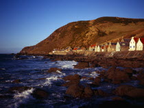 Scotland, Aberdeenshire, Crovie, One time fishing village seen from shoreline.  Row of cottages at foot of steep hillside overlooking coast and stone jetty.