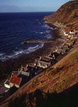 Scotland, Aberdeenshire, Crovie, One time fishing village seen from cliff top.  Row of cottages at foot of steep hillside overlooking coast and stone jetty.