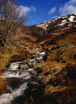 Scotland, Argyll and Bute, Loch Lubnaig, Loch Lomand and Trossachs National Park.  Mountain stream flows from west side of Benn Each, south of Loch Earn.  Patches of snow on mountainside beyond.
