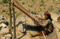 Nepal, East, Gudel, Woman sitting on ground to weave textile on hand loom.