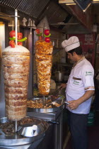 Turkey, Istanbul, Sultanahmet, man in kebab restaurant carving shawarma from skewered meats.