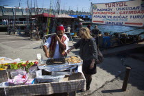 Turkey, Istanbul, Karakoy, Galata fish market, man selling freshly grilled fish served in a bread roll whilst talking on a mobile phone.