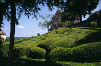 France, Aquitaine, Dordogne, Chateau de Marqueyssac near Vezac.  Exterior and gardens with clipped boxwood hedges and topiary.  Part framed by trees in foreground.