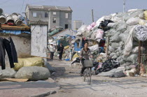 China, Jiangsu, Qidong, Female workers, one on a bicycle, leaving a  recycling depot, bundles of waste paper in plastic and polypropylene sacks.