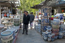 China, Jiangsu, Yangzhou, Ceramic pots for plants and decorative use in downtown canal-side street market. Man strolling through market looking at pots. Trees in background. Marco Polo once served as...