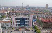 China, Jiangsu, Qidong, Bureau of Public Security with Chinese flag flying in forecourt and radio communications mast on the roof; red banners with Chinese characters hanging from building, City skyli...