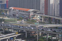 China, Shanghai , Light Railway train leaving Caoxi Road station in south Shanghai in the early morning with cars and buses at spaghetti junction, Apartment blocks in background with windows forming a...