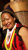 India, Nagaland, Lady from Naga Warrior tribe, with unique traditional costume and jewelry carrying a basket on her head.