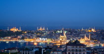 Turkey, Istanbul, View at sunset of illuminated city skyline from Beyoglu across rooftops to Galata Tower and Golden Horn with Galata Bridge leading to Sultanahmet with Haghia Sophia, New Mosque and B...