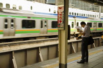 Japan, Honshu, Tokyo, Commuter on platform cooling himself with paper fan whilst waiting for his train.