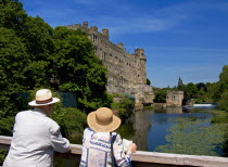 England, Warwickshire, Wawick Castle, couple looking at castle from bridge over the river Avon.