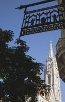 Hungary, Budapest, Buda Castle District: Matyas Church viewed from wrought iron traditional shop sign.