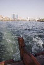 UAE , Dubai, Abra water taxi view from rudder across the Creek with Twin Towers shopping mall and skyline behind.