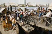 UAE , Dubai, Tourists board Abra water taxi moored on the Creek with Bur Dubai heritage skyline behind.