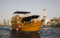 UAE , Dubai, restored traditional boat taking tourists on the Creek with Twin Towers shopping mall and skyline behind.