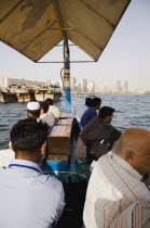 UAE , Dubai, Commuter passengers on Abra water taxi  on the Creek with Twin Towers shopping mall and skyline behind
