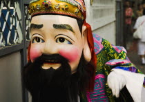 Thailand, Bangkok, Man in Chinese costume with papier-mache head and beard carried in parade celebrating local temple.