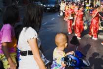 Thailand, Bangkok, Mother with three children on motorcycle watching parade celebrating local temple.