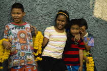 Thailand, Bangkok, Thai children with mobile phone and floral garlands to celebrate the annual blessing of local temple .