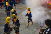 Thailand, Bangkok, Thai boys in Chinese character costume in dance troupe with firecrackers exploding at local temple.