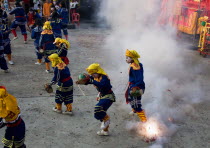 Thailand, Bangkok, Thai boys in Chinese character costume dancing and drumming with firecrackers exploding at local temple.