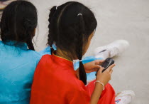 Thailand, Bangkok, Thai girl using mobile telephone seated with friend in costume of dance troupe.
