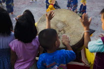 Thailand, Bangkok, Thai children bang drum while watching dance troupe with firecrackers exploding at local temple.