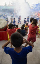 Thailand, Bangkok, Thai boys cover their ears watching performance with firecrackers exploding at local temple.