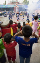 Thailand, Bangkok, Thai children bang drum while watching dance troupe with firecrackers exploding at local temple.