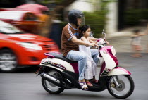 Thailand, Bangkok, Father with young daughter on motorcycle pass brightly coloured taxis.