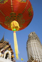 Thailand, Bangkok, Wat Yannawa temple roof and unfinished apartment block from 1990s Asian financial crash with red lanterns at Chinese New Year.