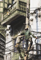 Thailand; Bangkok; Chinatown, Workmen, one in camouflage, repairing overhead cables in hot afternoon sun.