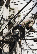 Thailand; Bangkok; Chinatown, Workman, in camouflage, repairing overhead cables in hot afternoon sun.