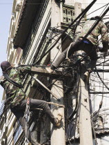 Thailand; Bangkok; Chinatown, Workmen, one in camouflage, repairing overhead cables in hot afternoon sun.