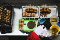 Thailand, Bangkok, Primary School girl in uniform at sausage stall outside BTS Skytrain station.